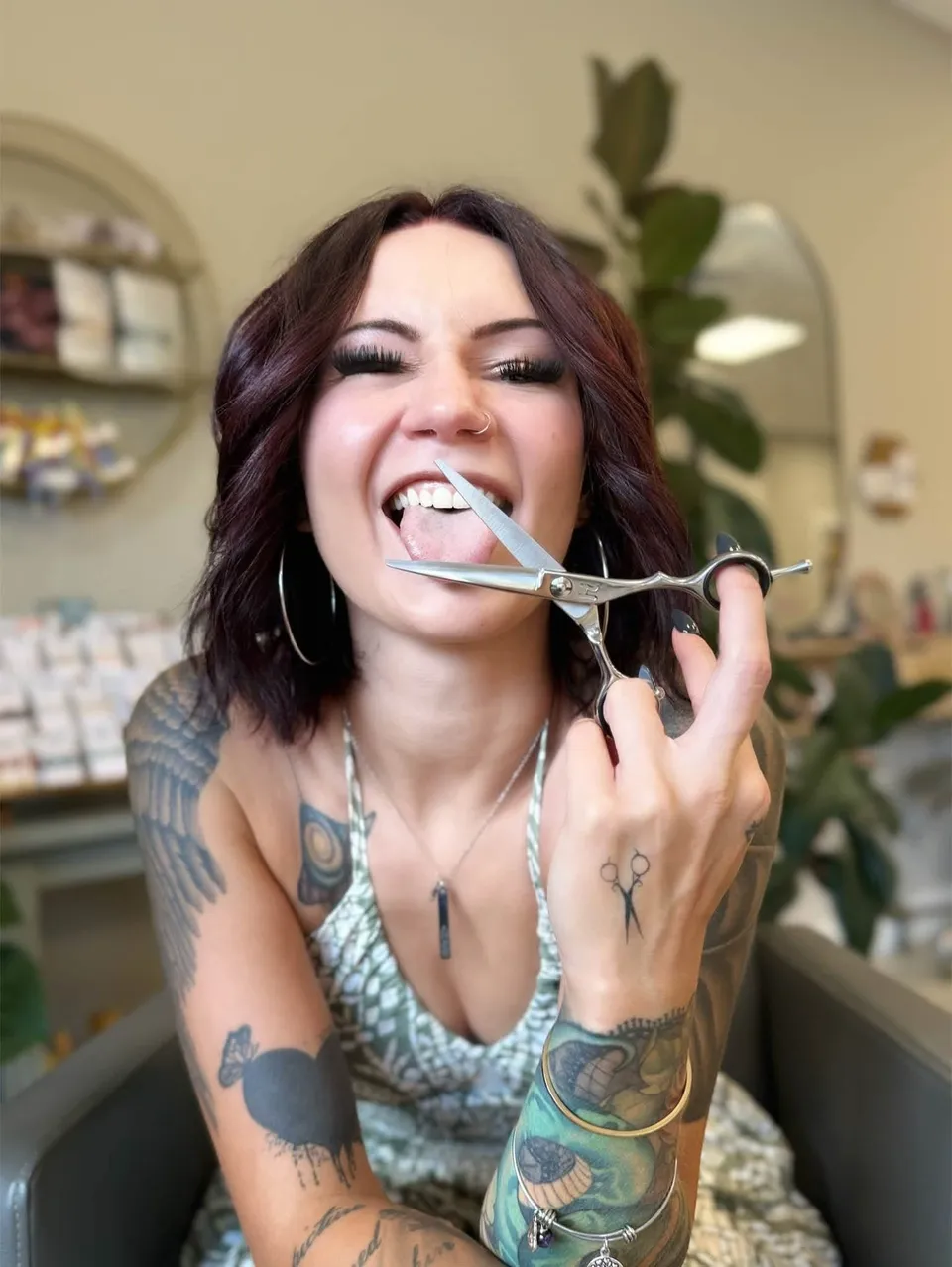 Em grinning with her tongue out, holding open shears up to the camera.